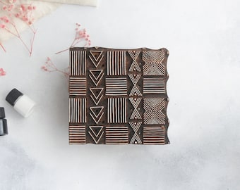May include: A wooden printing block with a geometric pattern of squares, triangles, and lines. The block is brown and the pattern is white. Two small bottles of paint are also in the image.