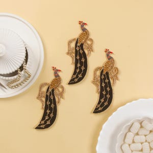 May include: Three gold and black peacock embroidery patches. The peacocks are facing to the right and have detailed embroidery with gold thread and black fabric.