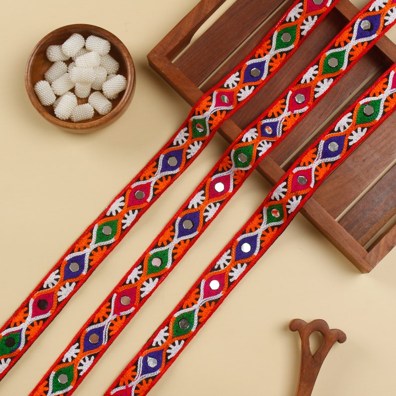 May include: Three strands of red trim with colorful embroidery and mirrored accents. The trim features a repeating pattern of white, orange, green, blue, and silver.