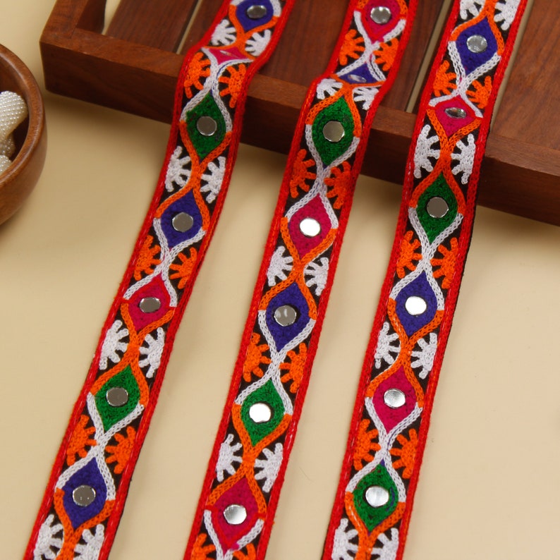 May include: Three strips of red, white, and black fabric trim with colorful embroidery and round, silver-toned mirrors. The trim is perfect for adding a touch of ethnic flair to clothing, home decor, or crafts.