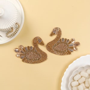 May include: Two gold swan-shaped embroidered patches with intricate details. The swans are facing opposite directions and have a beaded design.