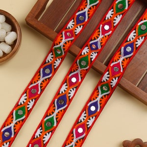Puede incluir: Tres galones de tela roja con bordados coloridos y detalles de espejo. Los galones presentan un patrón repetido de formas de diamante con hilo blanco, naranja, verde, azul y rosa.