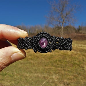 May include: Black macrame bracelet with a purple star-shaped gemstone in the center.