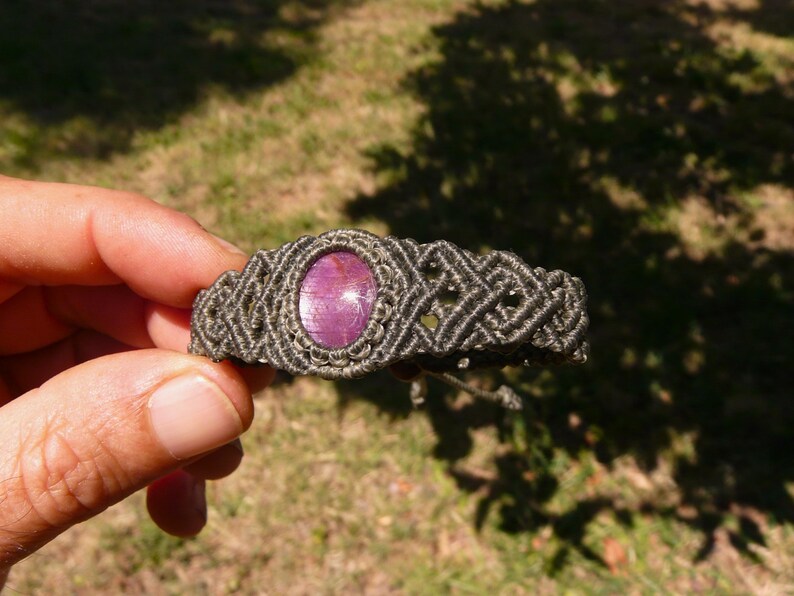 Bracciale a manetta intrecciato a mano in Macramè filato color grigio-verde con pietra naturale Rubino Stella vista lato destro primo piano su sfondo natura.