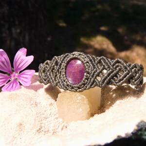 Bracciale a manetta intrecciato a mano in Macramè filato color grigio-verde con pietra naturale Rubino Stella vista lato sinistro esposto su minerale grezzo.