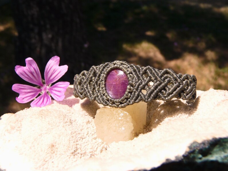 Bracciale a manetta intrecciato a mano in Macramè filato color grigio-verde con pietra naturale Rubino Stella vista lato sinistro esposto su minerale grezzo.