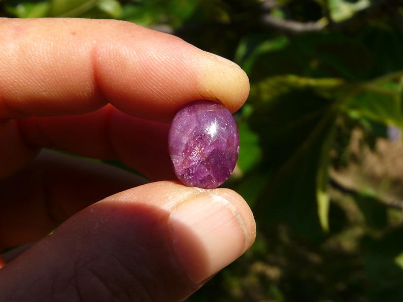 Pietra preziosa naturale Rubino Stella tenuto in mano su sfondo verde alla luce del sole.