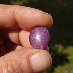 Pietra naturale Rubino Stella tenuto in mano, sullo sfondo prato verde.
