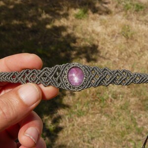 Bracciale a manetta intrecciato a mano in Macramè filato color grigio-verde con pietra naturale Rubino Stella vista bracciale aperto con dettaglio sull'intreccio geometrico in Macramè, primo piano su sfondo prato verde.