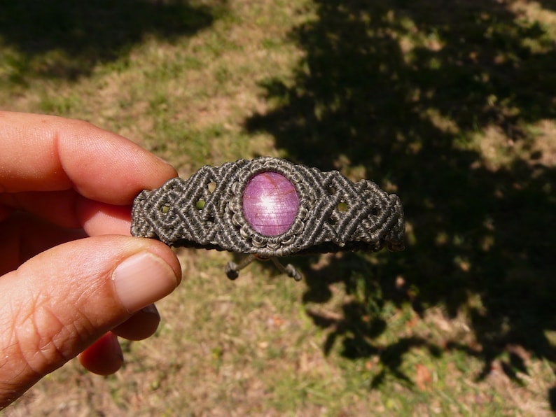 Bracciale a manetta intrecciato a mano in Macramè filato color grigio-verde con pietra naturale Rubino Stella vista centrale primo piano con sfondo prato verde.