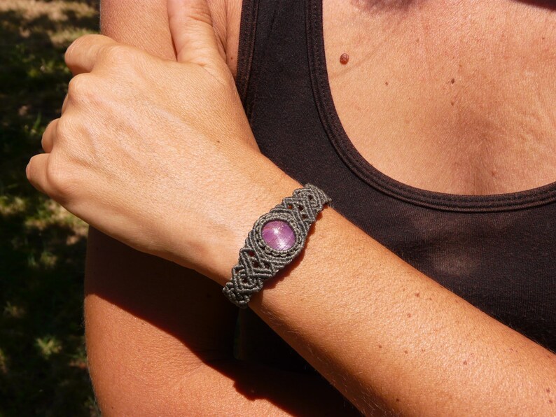 Bracciale a manetta intrecciato a mano in Macramè filato color grigio-verde con pietra naturale Rubino Stella, indossato da ragazza su sfondo naturale.