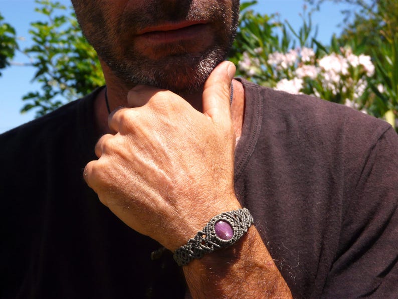 Bracciale a manetta intrecciato a mano in Macramè filato color grigio-verde con pietra naturale Rubino Stella primo piano indossato da uomo con maglia nera sullo sfondo fiori di Oleandro.