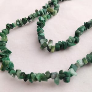 Puede incluir: Un collar de piedras preciosas verdes hecho de virutas de forma irregular. El collar está hecho de piedras naturales y es una pieza de joyería hermosa y única.