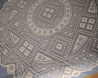 Könnte beinhalten: Eine weiße Häkeltischdecke mit einem runden Design in der Mitte. Die Tischdecke hat ein zartes Blumenmuster und einen gewellten Rand.