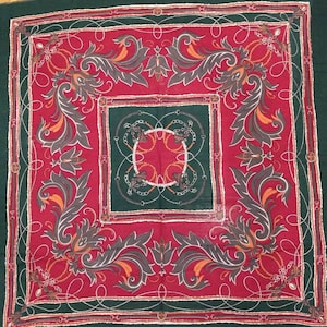 May include: A square green and red patterned fabric with a repeating design of stylized leaves and chains. The fabric has a dark green border and a red center with a smaller green square in the center.
