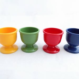Peut inclure: Quatre supports à œufs de différentes couleurs : jaune, vert, rouge et bleu. Chaque support a une base en piédestal.