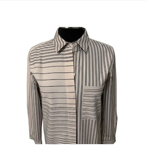 May include: A long-sleeved button-down shirt with a distinctive design. The shirt has a split design with alternating horizontal and vertical black stripes on a white background. A pocket on the left chest has horizontal stripes.