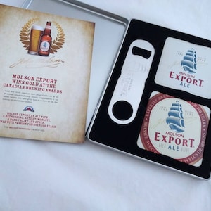 May include: A silver metal gift set with two coasters and a bottle opener. The coasters are round and feature a blue and white ship design with the text "Molson Export Ale". The bottle opener is silver and has the text "Molson Export" on it.