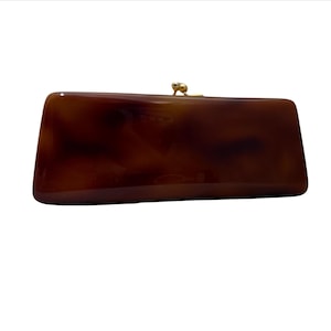 May include: A rectangular clutch bag featuring a glossy, dark brown and amber tortoiseshell pattern. The bag has a smooth, polished finish and is secured at the top center with a small, gold-toned metal kiss-lock clasp mechanism.