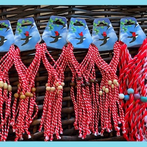 May include: A set of red and white string bracelets with wooden beads. The bracelets are tied together and have a swallow bird design on the packaging.