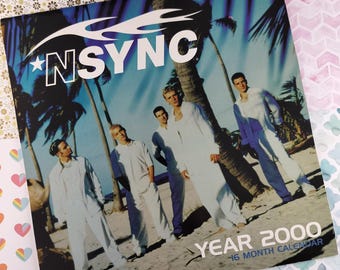 May include: A vintage 16-month calendar featuring a photo of the boy band *NSYNC. The band members are standing on a beach in front of palm trees. The calendar is titled "Year 2000".