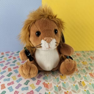 May include: A brown plush lion with a white face and a fluffy mane. The lion is sitting on a patterned surface.