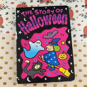 May include: A children's book titled "The Story of Halloween" with a black cover and pink background. The cover features a witch on a broom, a ghost, a black cat, and a bat. Stars and moons decorate the cover.