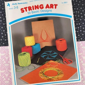 Puede incluir: Un kit vintage de "String Art" con un libro titulado "STRING ART 10 Basic Designs". La imagen muestra carretes de hilo colorido, ejemplos de diseños de arte con hilo y tijeras. El kit está diseñado para los grados 3-8.