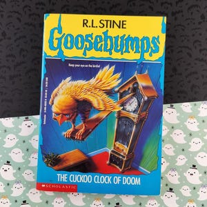 May include: A paperback book titled "Goosebumps: The Cuckoo Clock of Doom" by R.L. Stine. The cover features a yellow and blue design with a large illustration of a bird and a grandfather clock. The Scholastic logo is visible.