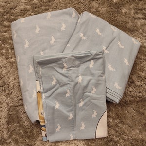 May include: A set of blue bedding with a white bunny pattern. The bedding includes a flat sheet, fitted sheet, and pillowcase.