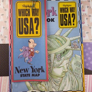 Puede incluir: Un libro amarillo y negro titulado "Which Way USA?" con un marcapáginas que presenta a un hombre de dibujos animados y el texto "Which Way USA? New York State Map".