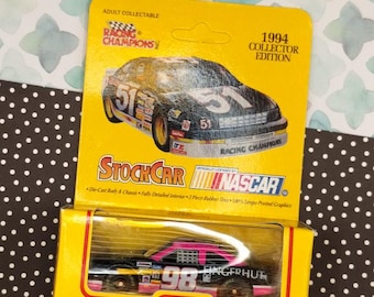 May include: A 1994 Racing Champions 1/64 scale die-cast replica stock car of the #98 Fingerhut car. The car is black with pink and yellow accents. The car is in a yellow and black box with the words "Racing Champions" and "NASCAR" on it.