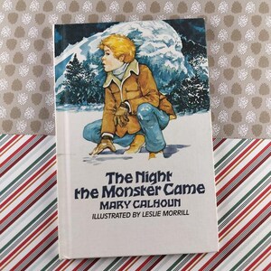 Peut inclure: Un livre à couverture rigide intitulé "The Night the Monster Came" de Mary Calhoun, illustré par Leslie Morrill. La couverture représente un enfant en veste marron et jean bleu dans une scène de montagne enneigée. Le livre est sur une surface à motifs.