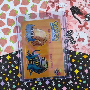 May include: A Pokemon card featuring Omanyte and Omastar, two Pokemon from the Kanto region. The card is yellow and orange with a blue and green illustration of the Pokemon. The card number is 1229.