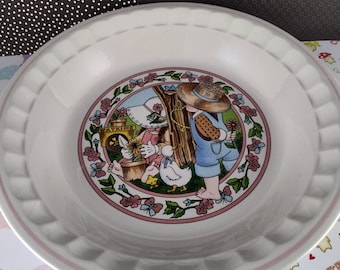 May include: A white ceramic bowl with a pink rim features a colourful illustration of a girl and a boy in a garden setting. The illustration includes flowers, butterflies, a birdhouse, and a rabbit. The bowl is ideal for serving soup, cereal, or snacks.