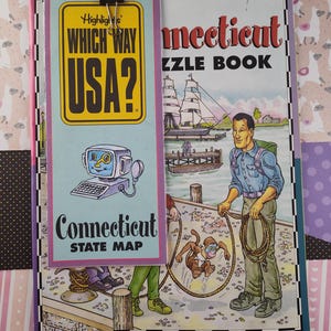 Puede incluir: Un libro azul y morado con el título "Connecticut Puzzle Book" y una ilustración de un barco y un hombre con un mono. El libro forma parte de la serie "Highlights Which Way USA?" e incluye un mapa del estado.