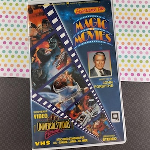May include: VHS video tape for "Experience the Magic of Movies" from Universal Studios Florida. The cover features images from various movies, the host John Forsythe, and the text "Souvenir Video".