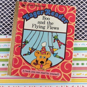 May include: A vintage children's book titled "Eager Reader Boo and the Flying Flews." The cover features a cartoon bear wearing a party hat, with illustrations of figures swinging. The book has a red and orange cover with the text "A book you can read by yourself."