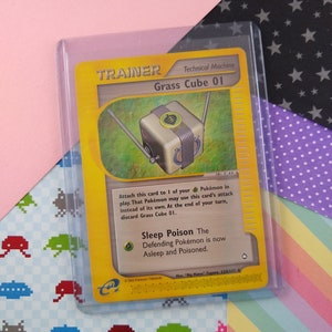 Puede incluir: Una carta de comercio de Pokemon amarilla y negra con una máquina técnica Grass Cube 01. La carta tiene una imagen de un cubo con una hoja verde en su interior. El texto de la carta dice: "Adjunta esta carta a 1 de tus Pokemon en juego. Ese Pokemon puede usar el ataque de esta carta en lugar del suyo propio. Al final de tu turno, descarta Grass Cube 01. Sueño Veneno El Pokemon defensor ahora está dormido y envenenado."