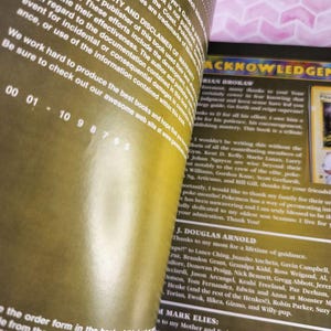 May include: Open book pages with text, including acknowledgements and copyright information. The pages have a yellowed appearance. The text includes names and thanks. The book is a guide for a trading card game.