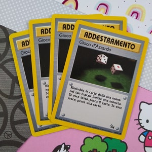 May include: Four yellow and silver trading cards with the text "Addestramento" and "Gioco d'Azzardo" on the top card. The cards are from the Pokemon Trading Card Game.