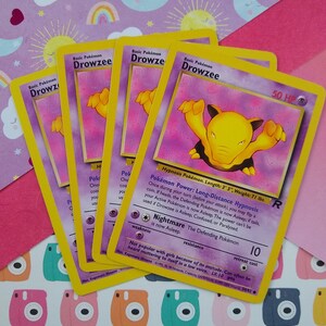 May include: A yellow and white Pokemon trading card featuring Drowzee, a hypnosis Pokemon. The card has a picture of Drowzee with its eyes closed and its arms raised. The card text describes Drowzee's abilities and stats. The card is in good condition.