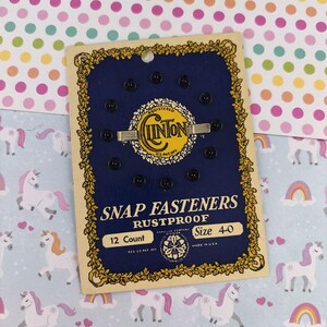 Puede incluir: Una tarjeta vintage de broches de presión negros, talla 4-0, con la marca "Clinton" en un diseño dorado y negro. La tarjeta dice "Snap Fasteners Rustproof 12 Count" y está hecha en los EE. UU.