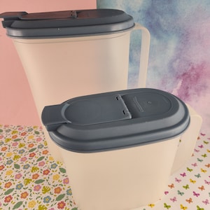 Può includere: Due brocche di plastica bianco sporco con coperchi blu scuro. Le brocche hanno manici e sono di dimensioni diverse. I coperchi hanno un design a ribalta. Lo sfondo è un mix di rosa, blu e motivi floreali.