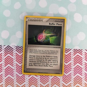 May include: A Pokémon Trainer card featuring a "Buffer Piece" tool. The card has a yellow border and includes text describing its function. The background is a colorful pattern.