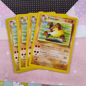 Puede incluir: Cuatro cartas de comercio de Pokémon amarillas que presentan a Primeape, una evolución de etapa 1 de Mankey. Las cartas tienen ilustraciones de Primeape, un Pokémon parecido a un mono marrón y amarillo con ojos rojos y una expresión feroz. Las cartas tienen texto que dice "Primeape", "Golpes de Furia", "Berrinche", "Debilidad", "Resistencia" y "Coste de Retirada".