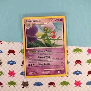 May include: A Pokemon trading card featuring Roserade, a Stage 1 Pokemon. The card has a yellow border and displays a colorful illustration of the character. The card is in a protective sleeve and is set against a patterned background.