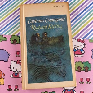 May include: Vintage hardcover book titled "Captains Courageous" by Rudyard Kipling. The cover features a blue illustration of two people in a boat on the water. The book has a cream-colored spine and is set against a colorful patterned background.