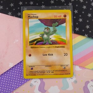 May include: A yellow and red Pokemon trading card featuring Machop, a green, muscular Pokemon with red eyes. The card has a picture of Machop lifting a large rock. The card text reads "Basic Pokemon Machop 50 HP" and "Superpower Pokemon. Length: 2' 7", Weight: 43 lbs."