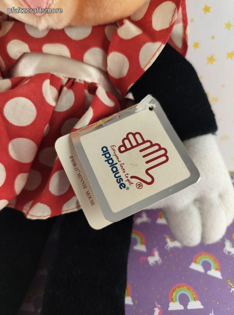 May include: A Minnie Mouse plush doll with a red and white polka dot dress. The doll has black pants, a white glove, and a tag that reads "Everyone loves to get applause&reg;". The tag also says "#8539 17" MINNIE MOUSE."